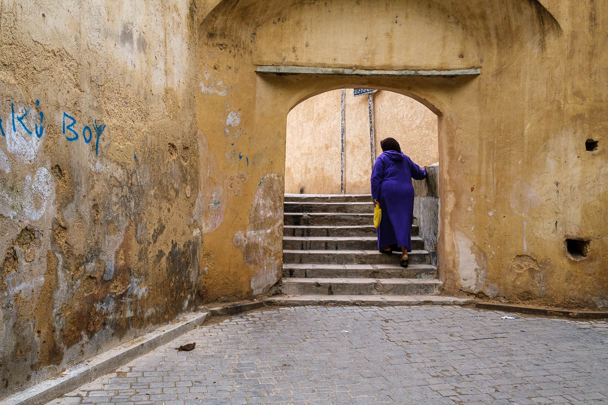 A traditional muslim lady walking through an arch in FES